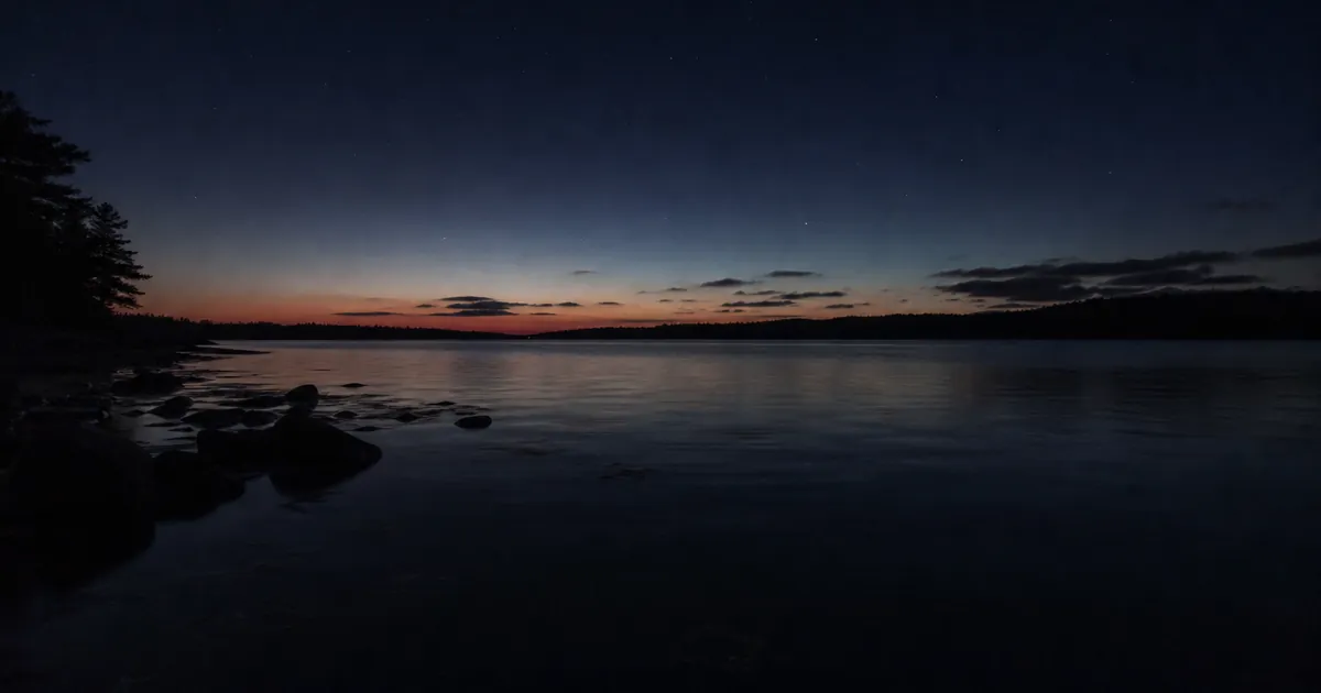 Mycket mörk höstnatt över en stilla vik med svaga stjärnor