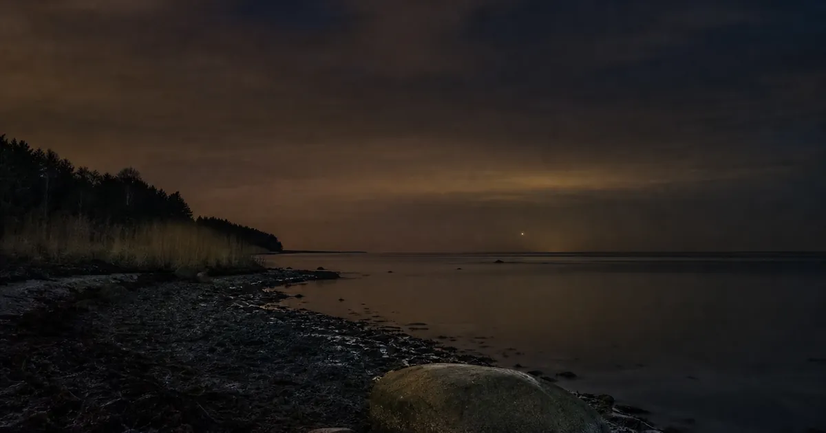 Höstnatt vid havet med en ljus stjärna precis över horisonten i dis