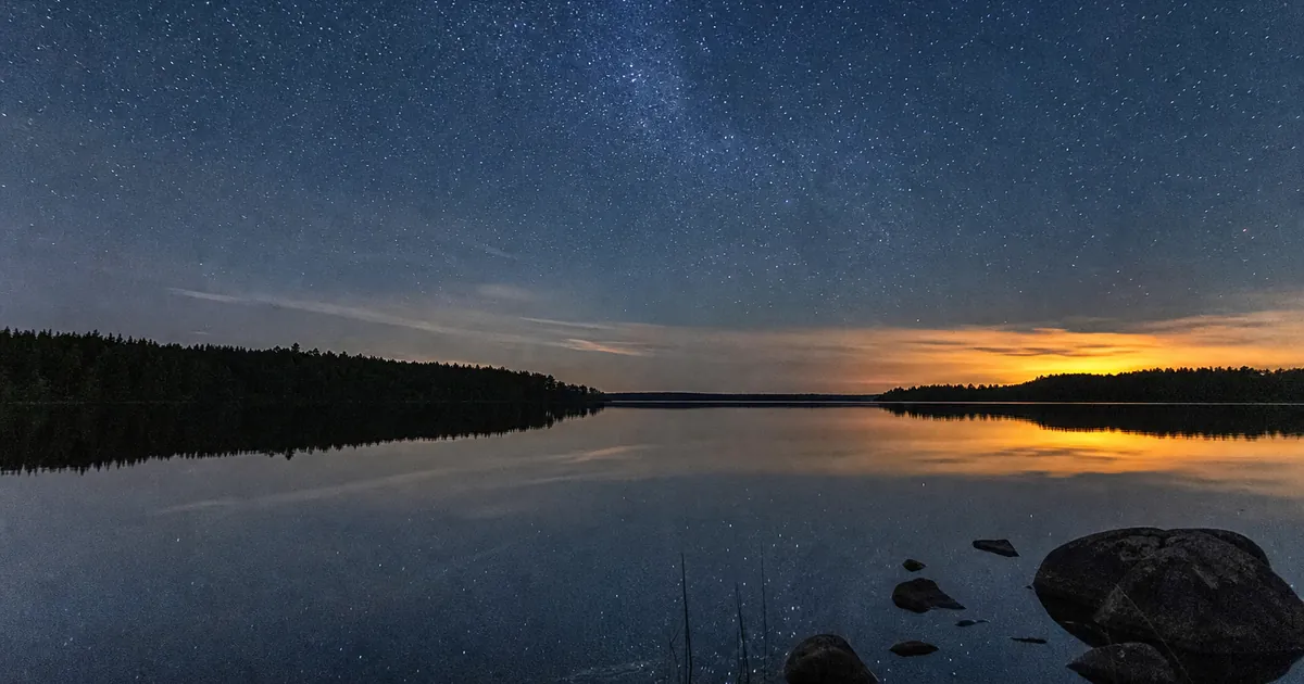 Sensommarnatt över en mörk sjö med rikt stjärnfält högt uppe