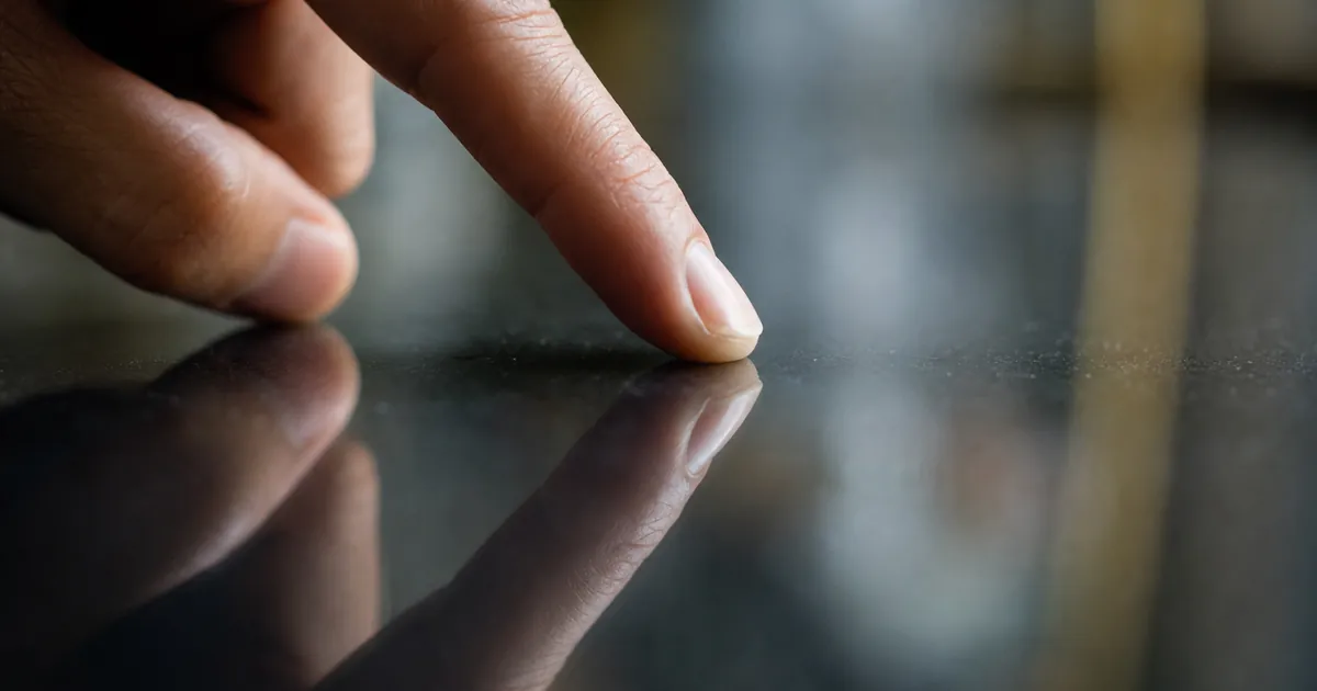 Fingertopp mot en mörk polerad glasyta i närbild