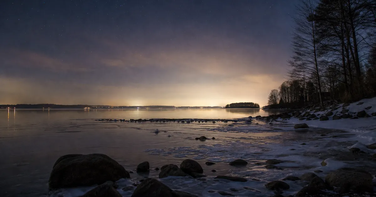 Senvinternatt över en stilla sjö med tunn is och svag stjärnhimmel