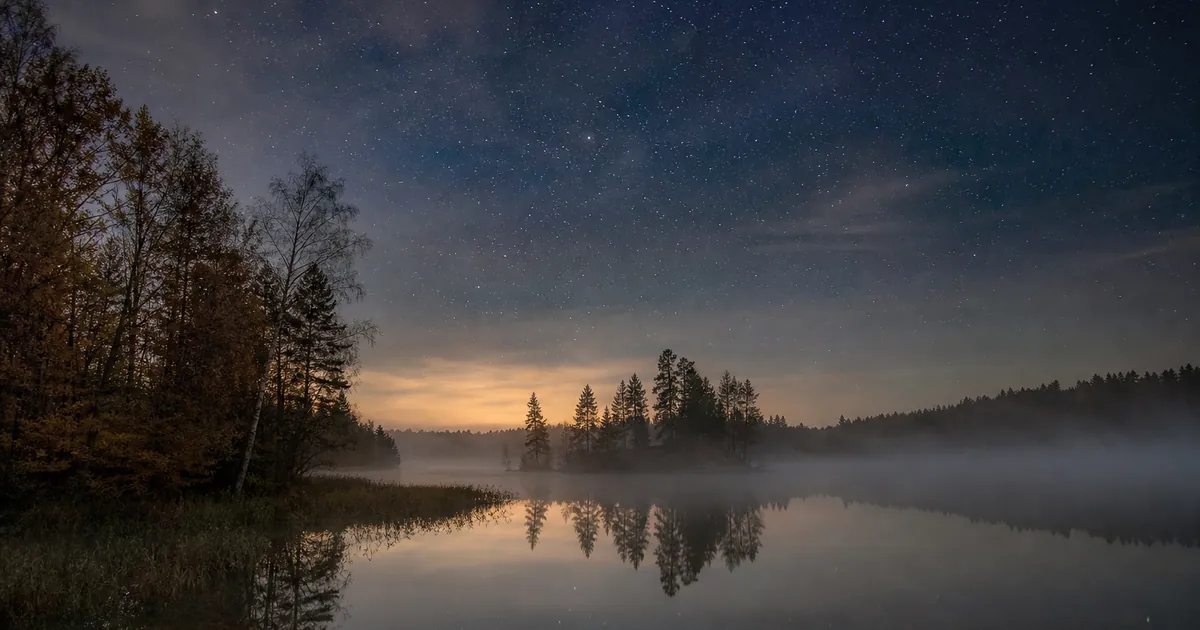 Dimmig höstnatt över en sjö med stjärnhimmel ovanför