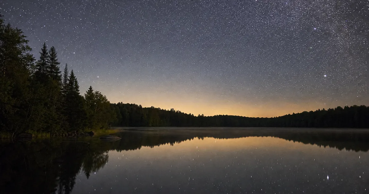 Sensommarnatt över en skogssjö med ett tätt band av svaga stjärnor