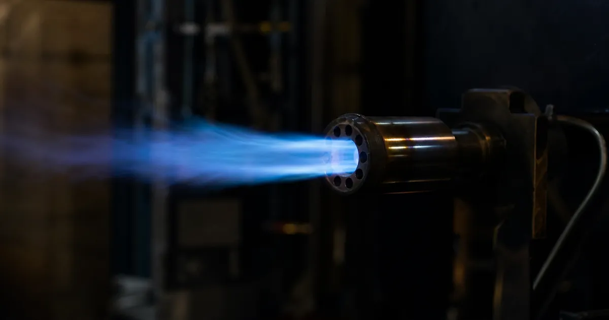 Blå låga vid ett metallmunstycke i en mörk verkstad